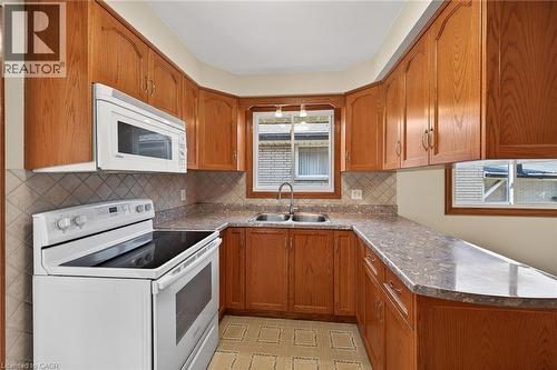 Kitchen featuring white appliances, a peninsula, wood finish cabinets, light floors, and dark countertops - 122 Glen Forest Drive, Hamilton, ON - Indoor Photo Showing Kitchen With Double Sink