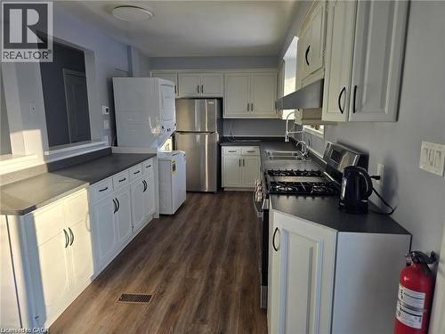 Kitchen with dark countertops, stainless steel appliances, white cabinets, dark wood-style floors, and stacked washer and dryer - 593 Mount Anne Drive, Waterloo, ON - Indoor Photo Showing Kitchen