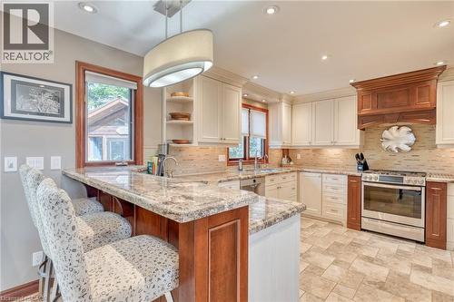Kitchen with stainless steel appliances, a peninsula, light stone counters, a kitchen breakfast bar, and backsplash - 15 Marquette Drive, Kitchener, ON - Indoor Photo Showing Kitchen With Upgraded Kitchen