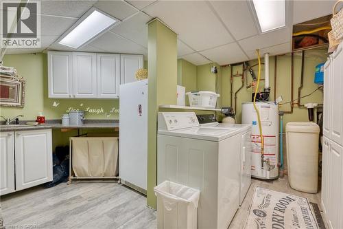 Laundry area featuring a drop ceiling, cabinet space, washer and clothes dryer, gas water heater, and light wood-style flooring - 15 Marquette Drive, Kitchener, ON - Indoor Photo Showing Laundry Room
