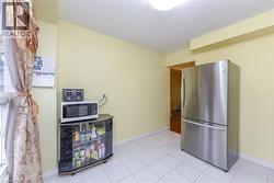 Kitchen featuring freestanding refrigerator, white microwave, and light tile patterned flooring - 