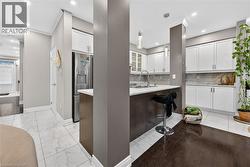 Kitchen with white cabinetry, stainless steel fridge with ice dispenser, light stone countertops, and decorative light fixtures - 