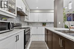 Kitchen with stainless steel appliances, glass insert cabinets, two tone cabinets, exhaust hood, and decorative backsplash - 