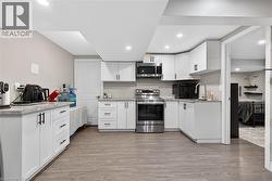 Kitchen featuring white cabinetry, stainless steel appliances, light wood finished floors, light stone countertops, and recessed lighting - 
