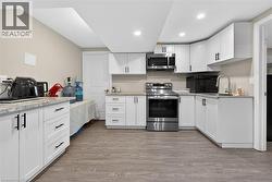 Kitchen with white cabinets, stainless steel appliances, light wood finished floors, light stone countertops, and recessed lighting - 