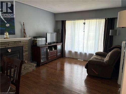 Living area featuring wood-finish flooring, a stone fireplace with a white mantel, and a large window - 56 Forsythe Avenue, Brantford, ON - Indoor Photo Showing Living Room With Fireplace