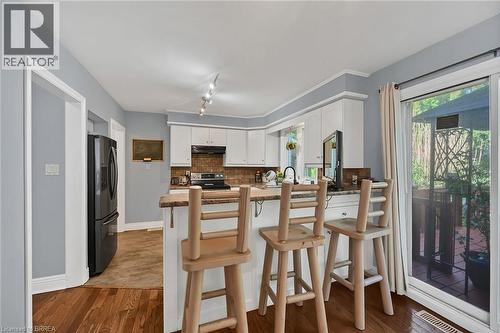 Kitchen with a peninsula, a kitchen breakfast bar, black fridge, white cabinets, and dark wood-style flooring - 56 Forsythe Avenue, Brantford, ON - Indoor