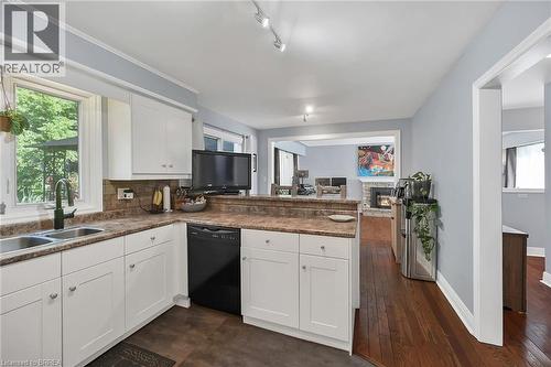 Kitchen with a peninsula, black dishwasher, white cabinets, a warm lit fireplace, and backsplash - 56 Forsythe Avenue, Brantford, ON - Indoor Photo Showing Kitchen With Double Sink