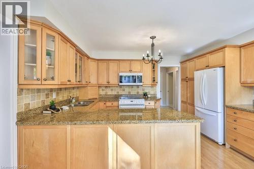 Kitchen featuring glass fronted cabinets, white appliances, light stone countertops, a peninsula, and light wood finish cabinets - 700 Fieldstone Road, Mississauga, ON - Indoor Photo Showing Kitchen With Double Sink