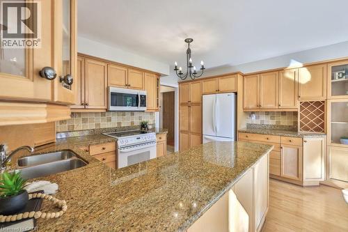 Kitchen featuring glass insert cabinets, dark stone counters, light wood finish cabinetry, white appliances, and a peninsula - 700 Fieldstone Road, Mississauga, ON - Indoor Photo Showing Kitchen With Double Sink