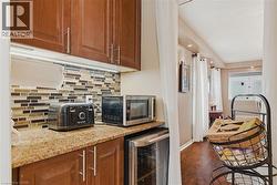 Kitchen featuring beverage cooler, wood finish cabinetry, light stone countertops, decorative backsplash, and recessed lighting - 