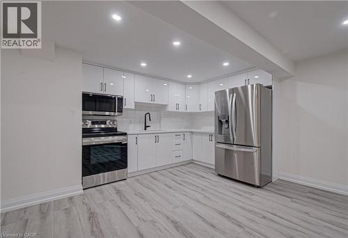 Kitchen featuring stainless steel appliances, light countertops, tasteful backsplash, white cabinets, and light wood-style flooring - 383 Rexford Drive Unit# 2, Hamilton, ON - Indoor Photo Showing Kitchen