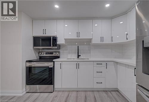 Kitchen featuring stainless steel appliances, white cabinets, light wood-style flooring, backsplash, and light stone counters - 383 Rexford Drive Unit# 2, Hamilton, ON - Indoor Photo Showing Kitchen