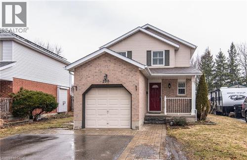 Traditional home featuring covered porch, asphalt driveway, brick siding, a front lawn, and a garage - 236 Dartmoor Crescent, Waterloo, ON - Outdoor