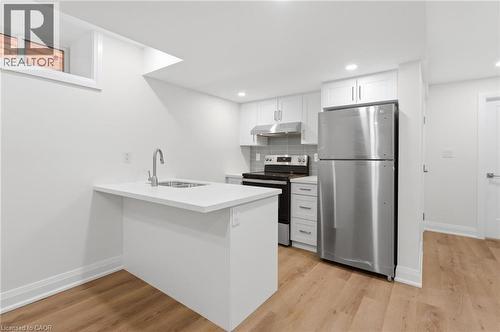 Kitchen featuring stainless steel appliances, white cabinetry, a peninsula, light wood-style flooring, and backsplash - 187 Oak Avenue Unit# Lower, Hamilton, ON - Indoor Photo Showing Kitchen