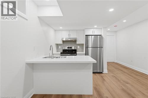 Kitchen with stainless steel appliances, a peninsula, white cabinets, light wood finished floors, and backsplash - 187 Oak Avenue Unit# Lower, Hamilton, ON - Indoor Photo Showing Kitchen With Double Sink