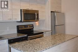 Kitchen with stainless steel appliances, light stone countertops, and white cabinetry - 