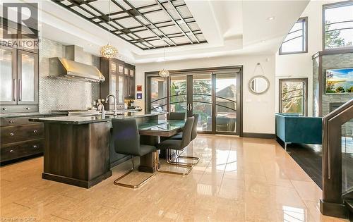 Kitchen featuring an island with sink, glass fronted cabinets, dark wood finish cabinets, a tray ceiling, and decorative backsplash - 24 Jacob Gingrich Drive, Kitchener, ON - Indoor