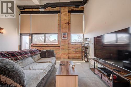 Living area featuring a high ceiling, brick wall, and carpet flooring - 85 Spruce Street Unit# 103, Cambridge, ON - Indoor