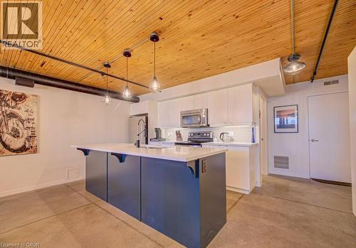 Dual tone kitchen with decorative light fixtures, a kitchen island with sink, stainless steel microwave, wooden ceiling, and black range with electric cooktop - 85 Spruce Street Unit# 103, Cambridge, ON - Indoor Photo Showing Kitchen
