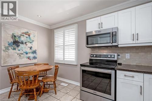 Kitchen with stainless steel appliances, white cabinetry, crown molding, light tile patterned flooring, and dark stone countertops - 220 Townsend Avenue, Burlington, ON - Indoor