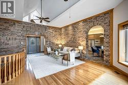 Living area featuring light wood-type flooring, a high ceiling, ceiling fan, arched walkways, and brick wall - 