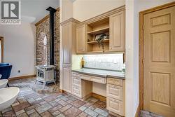 Bar area with built in desk, a wood stove, dark stone counters, light wood finish cabinetry, and open shelves - 