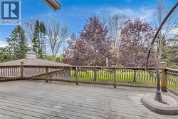Spacious outdoor deck featuring wood-finish flooring, a decorative wood railing with ornate balusters, and expansive green space - 