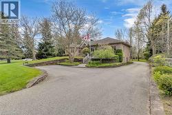 Brick exterior with a stone retaining wall, mature trees, and a paved driveway leading to the entrance - 