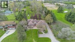 Expansive property featuring a stone-clad residence with a multi-level roofline, a circular driveway, mature trees, and a substantial green lawn - 
