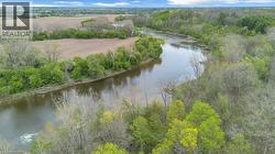 Meandering river bordered by lush, mature trees and open fields - 