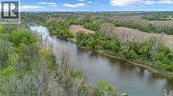Winding river surrounded by abundant mature trees and undeveloped fields, with distant urban structures visible under a partly cloudy sky - 