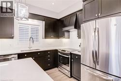 Kitchen featuring stainless steel appliances, hanging light fixtures, light wood-style floors, and light stone counters - 