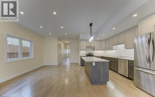 Dual tone kitchen featuring stainless steel appliances, light countertops, light wood-type flooring, a kitchen island, and pendant lighting - 113 Walter Street, Kitchener, ON - Indoor Photo Showing Kitchen With Upgraded Kitchen