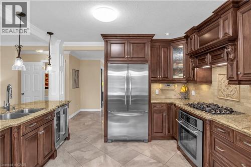Kitchen with stainless steel appliances, light stone countertops, ornamental molding, hanging light fixtures, and glass insert cabinets - 228 Michener Crescent, Kitchener, ON - Indoor Photo Showing Kitchen With Double Sink With Upgraded Kitchen