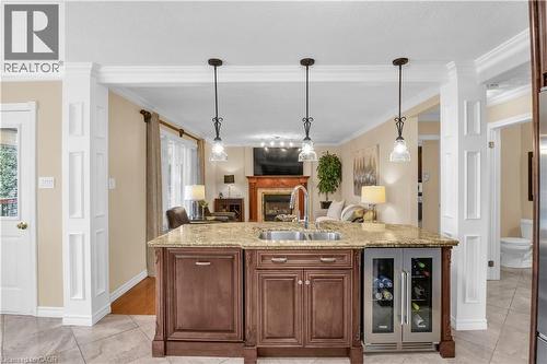 Bar featuring wine cooler, decorative light fixtures, light stone countertops, crown molding, and a fireplace - 228 Michener Crescent, Kitchener, ON - Indoor Photo Showing Kitchen With Double Sink