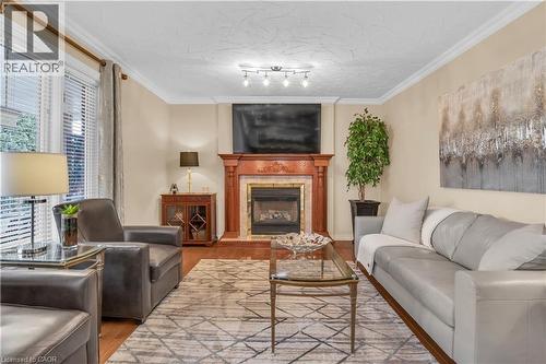 Living room with ornamental molding, wood finished floors, a fireplace with raised hearth, and a textured ceiling - 228 Michener Crescent, Kitchener, ON - Indoor Photo Showing Living Room With Fireplace