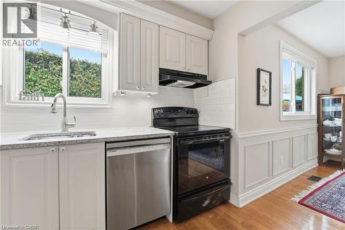 Kitchen featuring black / electric stove, dishwasher, a wainscoted wall, light wood-style flooring, and light stone counters - 668 Tomahawk Crescent, Ancaster, ON - Indoor Photo Showing Kitchen