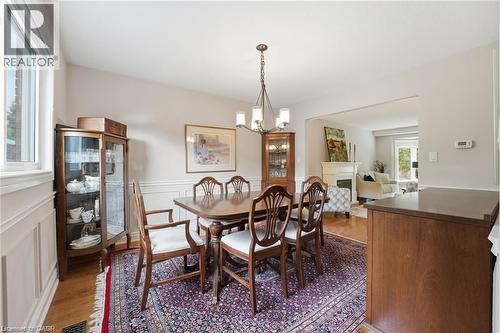 Dining room with a fireplace, light wood-style flooring, a decorative wall, a chandelier, and a wainscoted wall - 668 Tomahawk Crescent, Ancaster, ON - Indoor Photo Showing Dining Room