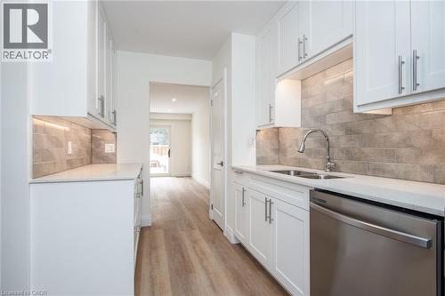 Kitchen featuring stainless steel dishwasher, white cabinets, light stone countertops, light wood finished floors, and tasteful backsplash - 27 Queenston Drive, Kitchener, ON - Indoor Photo Showing Kitchen With Double Sink