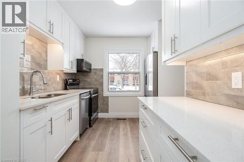Kitchen featuring white cabinetry, light stone counters, stainless steel appliances, light wood finished floors, and tasteful backsplash - 27 Queenston Drive, Kitchener, ON - Indoor Photo Showing Kitchen With Double Sink