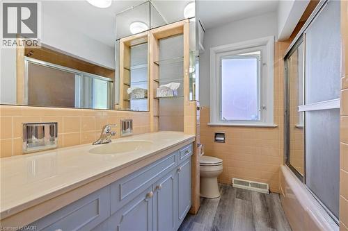 Full bath with vanity, bath / shower combo with glass door, dark wood-type flooring, and tile walls - 40 Bertram Drive, Dundas, ON - Indoor Photo Showing Bathroom