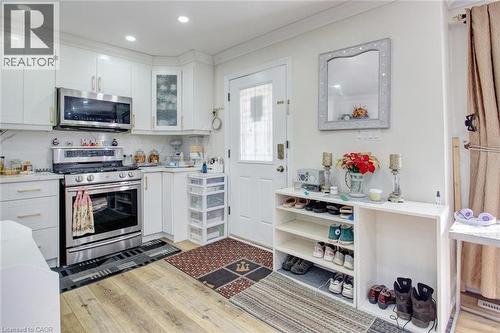 Kitchen with stainless steel appliances, light wood-type flooring, white cabinets, glass fronted cabinets, and decorative backsplash - 823 Queensdale Avenue E, Hamilton, ON - Indoor Photo Showing Kitchen