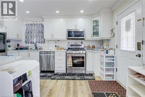 Kitchen featuring white cabinets, stainless steel appliances, light wood-type flooring, decorative backsplash, and light stone countertops - 823 Queensdale Avenue E, Hamilton, ON - Indoor Photo Showing Kitchen With Upgraded Kitchen