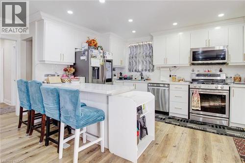 Kitchen featuring wood-finish flooring, white cabinetry, a central island with countertop seating, stainless steel appliances, and recessed lighting - 823 Queensdale Avenue E, Hamilton, ON - Indoor Photo Showing Kitchen With Upgraded Kitchen