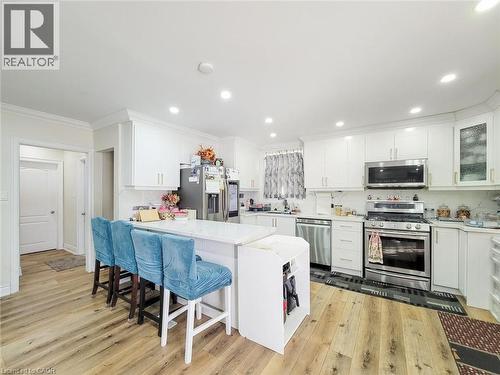 Kitchen featuring white cabinetry, wood-finish flooring, recessed lighting, a built-in stainless steel microwave, and a central island with a solid surface countertop - 823 Queensdale Avenue E, Hamilton, ON - Indoor
