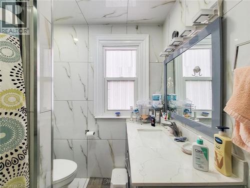 Bathroom featuring a framed mirror, a vanity with an integrated sink, a window with white trim, a toilet, and full-height wall tiling - 823 Queensdale Avenue E, Hamilton, ON - Indoor Photo Showing Bathroom