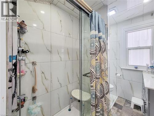 Shower enclosure featuring a sliding glass door and white marble-look wall tiling - 823 Queensdale Avenue E, Hamilton, ON - Indoor Photo Showing Bathroom