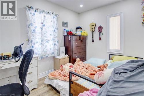 Bright interior space featuring light-colored walls, wood-finish flooring, a rectangular window with white trim, and a second narrow vertical window - 823 Queensdale Avenue E, Hamilton, ON - Indoor Photo Showing Bedroom