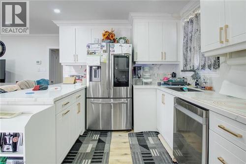 Kitchen featuring stainless steel appliances, ornamental molding, white cabinets, a peninsula, and light wood-type flooring - 823 Queensdale Avenue E, Hamilton, ON - Indoor Photo Showing Kitchen